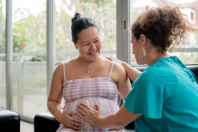 Silvia feeling the baby's movements in a pregnant woman's belle as she smiles.