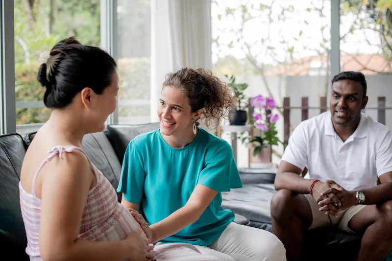 Silvia smiling and talking to a pregnant woman as her husband watches.