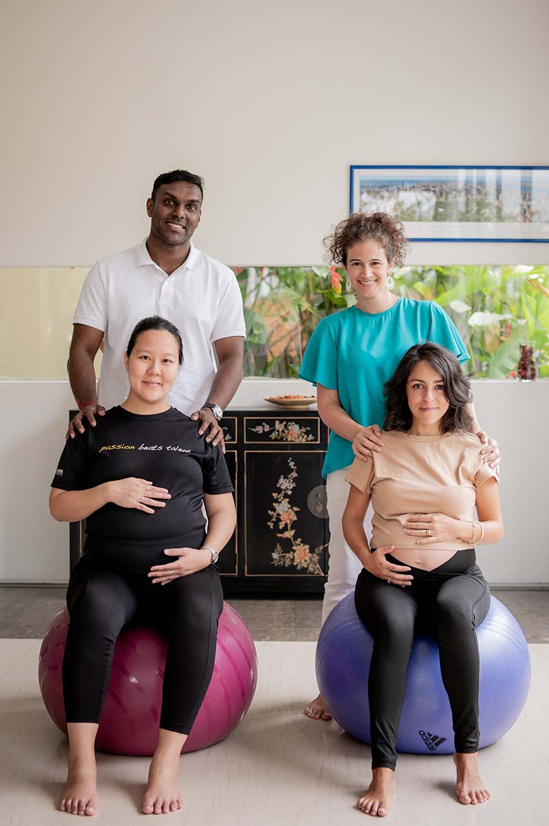 Two pregnant women sitting on exercise balls, with Silvia and one of their husbands behind them.